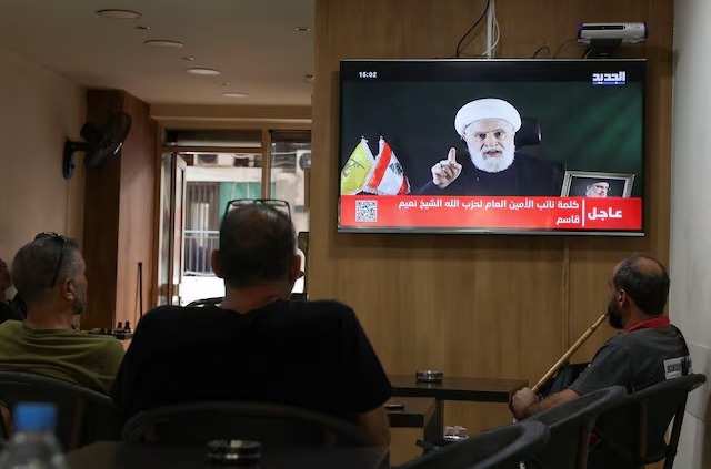 Orang-orang menyaksikan Wakil Pemimpin Hezbollah, Sheikh Naim Qassem, menyampaikan pidato yang disiarkan di televisi, saat mereka duduk di sebuah kafe di Beirut, Lebanon, 15 Oktober 2024. REUTERS/Mohamed Azakir