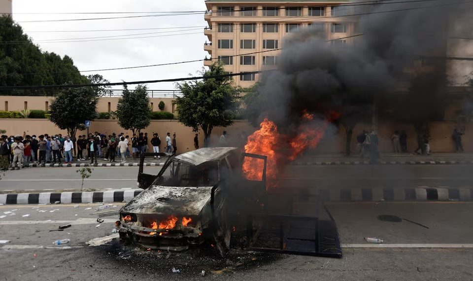 Orang-orang berdiri di dekat sebuah kendaraan yang dibakar oleh para demonstran saat aksi protes menentang korupsi dan keputusan pemerintah memblokir sejumlah platform media sosial, di Kathmandu, Nepal, 8 September. Sumber foto : REUTERS